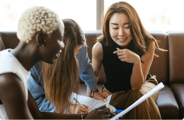 Three women chatting and laughing over documents.