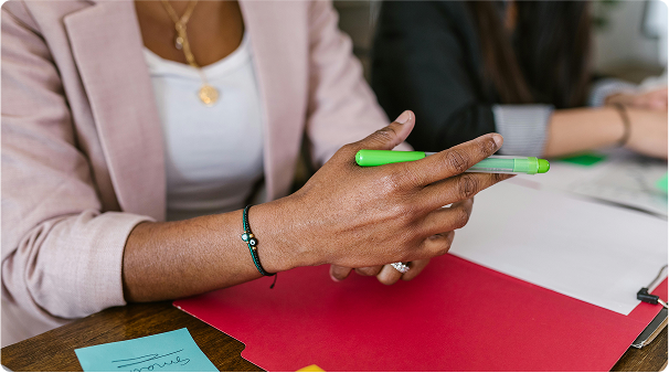 A person holding a green pen in their hand over a red folder