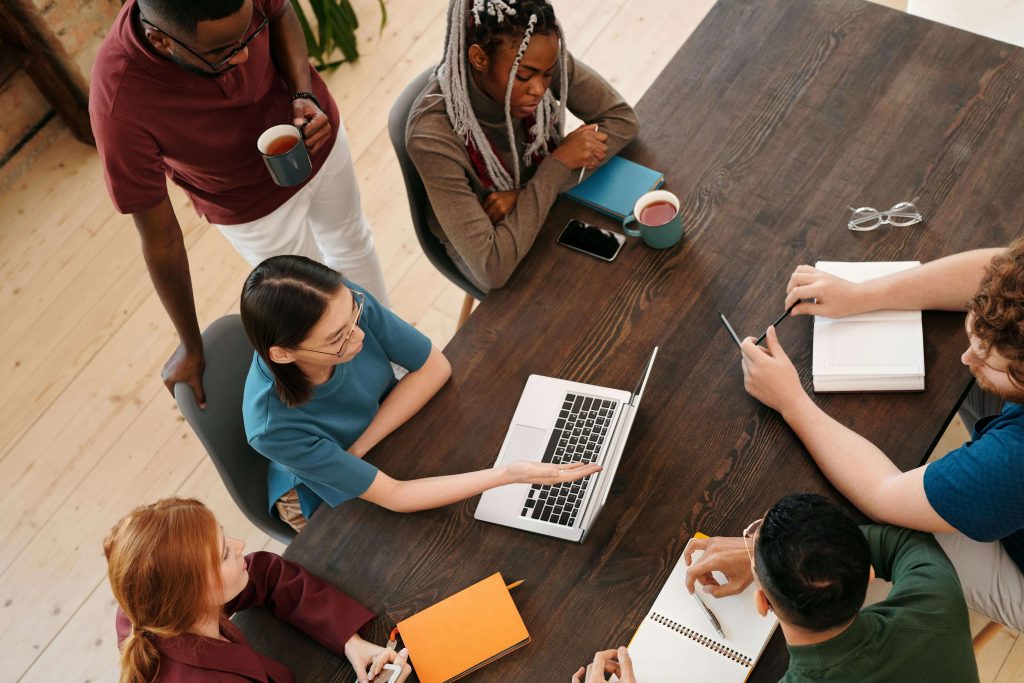 an overhead view of people sitting around a table looking a laptop brainstorming ideas